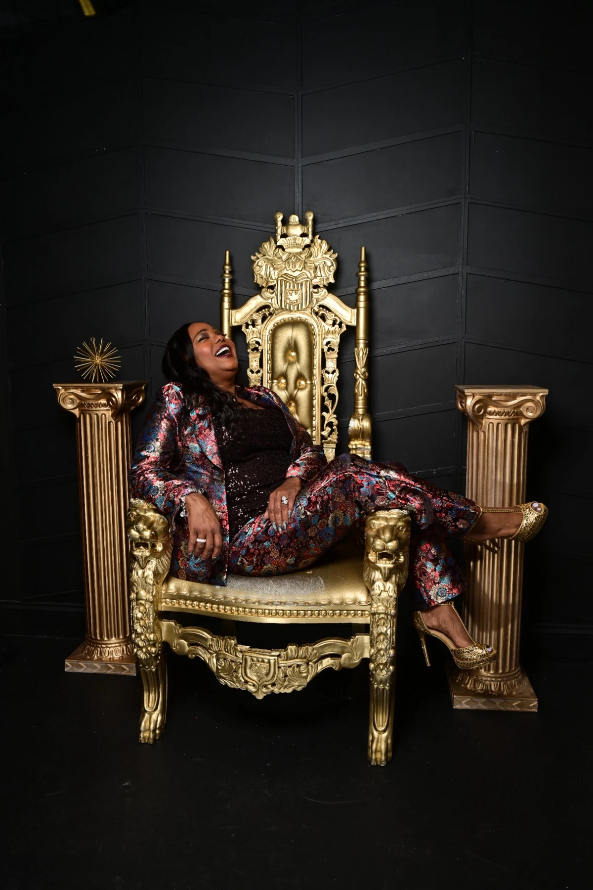 Cocoa Brown in a patterned suit on a gold throne